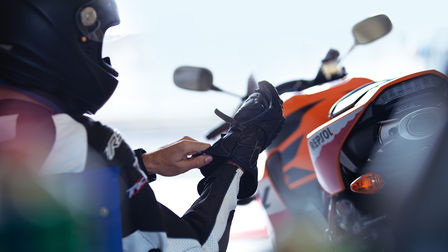 A motoros megigazítja a kesztyűjét. Motorkerékpár hátulról a motoros jobbján.